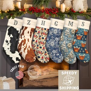 May include: Six Christmas stockings with personalized letters hang above a fireplace. The stockings feature various patterns, including cowhide, floral, and highland cow designs. The stockings have white cuffs and are decorated with festive greenery.