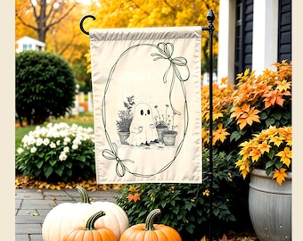 May include: A rectangular garden flag featuring a cream-colored background with a dark green line-art illustration of a ghost holding a mug, surrounded by potted plants and enclosed within an oval frame decorated with two tied bows at the corners.