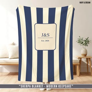 May include: Navy and cream striped sherpa blanket with a personalized center. The center features the initials "J&S" and the year "Est. 2026". The blanket is displayed indoors.