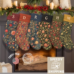 May include: Six Christmas stockings with floral patterns and personalized letters hang above a fireplace. The stockings have different colored tops: burgundy, rust, navy, black, olive, and gold. The stockings are decorated with flowers.