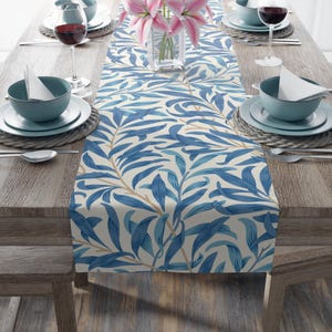 May include: A blue and white floral table runner with a repeating pattern of leaves. The runner is laid on a wooden table with place settings on either side.