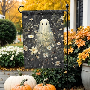 May include: A Halloween garden flag featuring a ghost figure amidst white flowers and greenery against a dark background. The flag is displayed outdoors with pumpkins and fall foliage in the foreground.