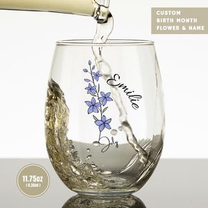 May include: A clear stemless wine glass with a capacity of 11.75oz, featuring a purple birth month flower illustration, the name Emilie, and the text July. Liquid is being poured into the glass, which also displays the text Custom Birth Month Flower & Name.