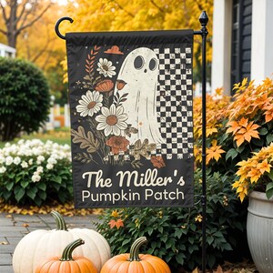 Puede incluir: Bandera de jardín negra de Halloween con una ilustración de fantasma, flores y un patrón de cuadros. El texto "The Miller's Pumpkin Patch" está en la bandera. Calabazas y follaje otoñal en primer plano.