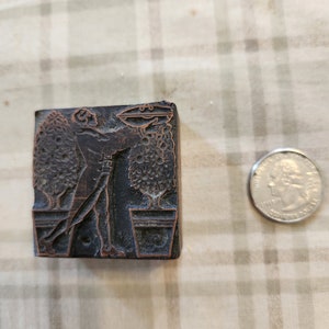 May include: A vintage woodblock printing stamp with a design of a person tending to two potted plants. The stamp is made of dark brown wood and has a worn, antique look.
