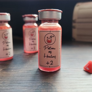 May include: Three small glass bottles filled with a red liquid and labeled "Potion of Healing +2". The bottles are on a wooden surface with two red dice.