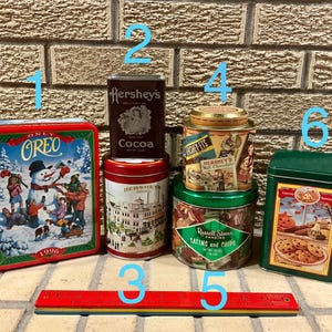 Op de afbeelding: Een verzameling vintage blikken, waaronder een Oreo-blik uit 1996, Hershey's cacao en diverse snoepblikken. Onderaan ligt een rode en gele liniaal. De blikken zijn geplaatst tegen een bakstenen muur.