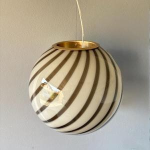 May include: A spherical pendant light fixture with a gold-colored metal ring and a clear glass globe. The globe features a pattern of alternating cream and dark brown stripes. The light hangs from a thin, clear wire.