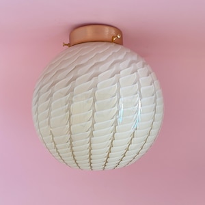 May include: A spherical, cream-coloured ceiling light with a textured, layered pattern. It features a copper-toned base and small gold details. The light is mounted on a pink ceiling.