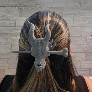 May include: A gray dragon head hair clip with a bone-shaped stick attached. The clip is in a person's hair.