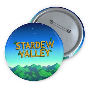 May include: A round button with a blue sky and green mountains background. The text "STARDEW VALLEY" is in gold letters with green leaves on either side.