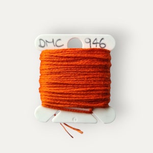 May include: A spool of orange DMC 946 embroidery thread. The white plastic spool is labelled with the DMC logo and the number 946. The text "Bailey Whin Supplies" is at the bottom of the image.