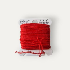 May include: A spool of bright red DMC 666 embroidery floss. The floss is wound around a white plastic bobbin. The text "DMC 666" is printed on the bobbin. The words "Bailey Whin Supplies" are printed below the bobbin.
