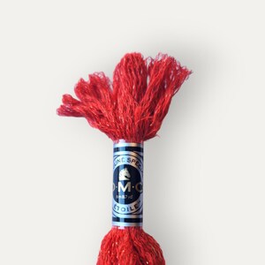 May include: A spool of red embroidery floss with gold glitter. The DMC brand label is visible on the spool. The label is black with white text and a gold horse logo.
