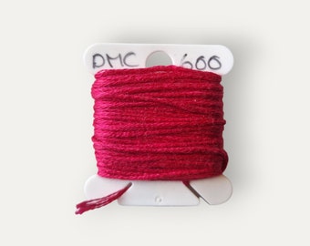 May include: A spool of DMC embroidery floss in color 600, a deep red. The floss is wound on a white plastic spool with the DMC logo and number printed on it.
