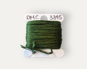 May include: A spool of DMC embroidery floss in a dark green color, labeled with the number 3345. The floss is wound on a white plastic spool with a label that says "DMC".