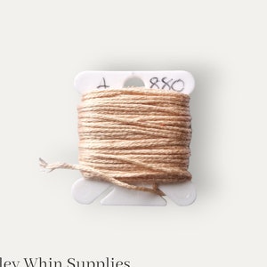 May include: A spool of beige embroidery floss wound on a white plastic bobbin with the number "880" written on it.