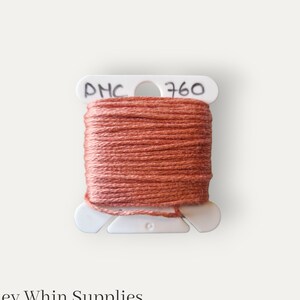 Könnte beinhalten: Eine Spule mit DMC-Stickgarn in Farbe 760, einem gedämpften Orange-Braun-Ton. Das Garn ist auf einer weißen Kunststoffspule gewickelt, auf der das DMC-Logo und die Farbnummer aufgedruckt sind.