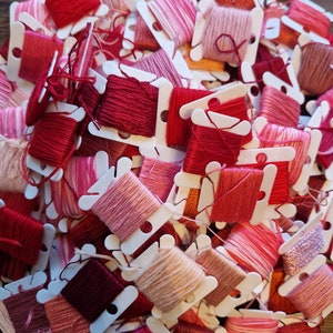Könnte beinhalten: Ein großer Haufen von Stickgarn-Spulen in verschiedenen Rosatönen und Rottönen. Die Spulen sind in einem zufälligen Muster angeordnet und alle in weißen Plastikbehältern.