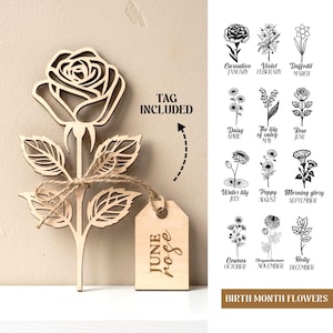 Op de afbeelding: Een houten roos met gedetailleerde uitsparingen, vastgebonden met touw, en een label met de tekst "June Rose". De afbeelding bevat ook een overzicht van geboortebloemen, zoals anjer, viooltje en narcis. De tag is inbegrepen.