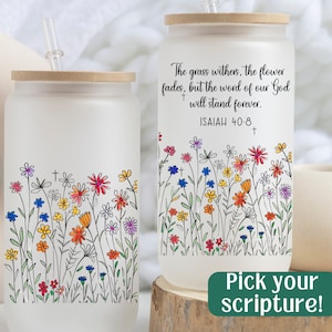 May include: Two white frosted glass tumblers with bamboo lids and straws. The tumblers feature a colorful floral design and a scripture quote from Isaiah 40:8. The quote reads "The grass withers, the flower fades, but the word of our God + will stand forever. ISAIAH 40:8 +"