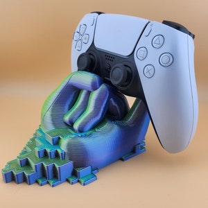 Op de afbeelding: Een 3D-geprinte, blauwe en groene gepixelde hand die een witte PlayStation 5-controller vasthoudt.