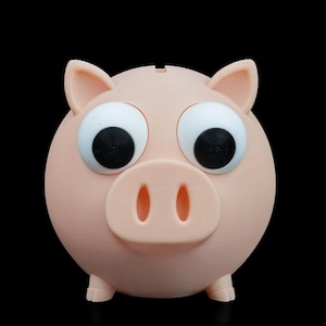 Puede incluir: Una alcancía rosa claro con ojos grandes y caricaturescos y un pequeño hocico. La alcancía tiene una ranura en la parte superior para insertar monedas y pequeños pies. El fondo es negro sólido.