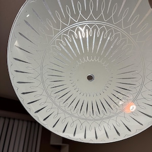 May include: A frosted glass ceiling light fitting with an etched decorative design. The design features curved lines and elongated teardrop shapes radiating from the centre. The fitting has a single hole in the centre.