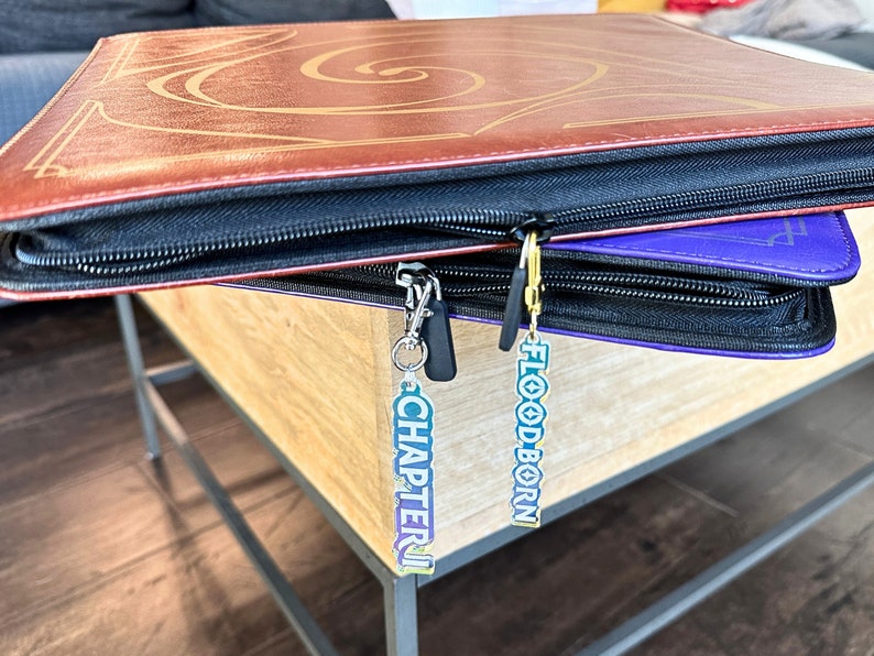 Zipper Pulls to organize Lorcana TCG binders in iridescent color. Available for Lorcana, Chapter 1, Floodborn, Inkands, and Ursula set names and in gold and silver clasps