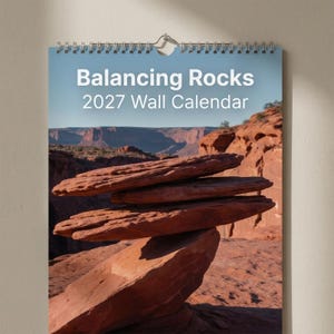 May include: A 2027 wall calendar with a spiral binding at the top. The cover features a photograph of red sandstone rocks balanced on top of each other in a desert landscape. The white text on the cover reads Balancing Rocks 2027 Wall Calendar.