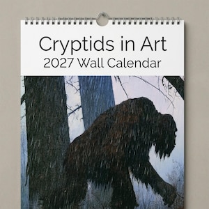 Puede incluir: Un calendario de pared 2027 titulado Cryptids in Art. La sección superior presenta texto negro sobre fondo blanco. La sección inferior muestra una criatura oscura, peluda y simiesca caminando por un bosque lluvioso con tonos azules.