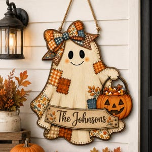 May include: A hanging wooden ghost sign featuring a plaid bow, patchwork patterns in orange and brown, and a jack-o'-lantern bucket filled with candy corn. A banner across the bottom displays the text The Johnsons in black cursive script.