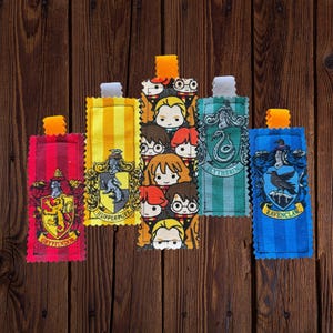Op de afbeelding: Set van vijf Harry Potter huis-thema stof bookmarks. Elke bookmark heeft een ander huiswapen en personages uit de boeken. De bookmarks zijn in de kleuren van elk huis: rood en goud voor Griffoendor, geel en zwart voor Huffelpuf, groen en zilver voor Zwadderich, en blauw en brons voor Ravenklauw.