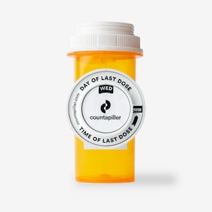 May include: A white pill bottle with a white, round, rotating label that says "Day of Last Dose" and "Time of Last Dose". The label also has the word "WED" and the logo "countapiller.com".