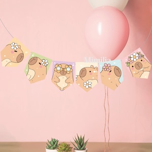 Puede incluir: Una guirnalda con capibaras ilustrados con coronas de flores y gafas de sol, colgada entre dos globos. La guirnalda está hecha de banderines coloridos sobre un fondo rosa claro. Tres pequeñas suculentas en macetas están en la parte inferior.