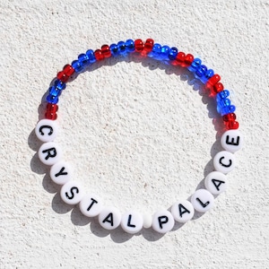 Könnte beinhalten: Ein Armband mit roten und blauen Perlen, auf dem "CRYSTAL PALACE" in weißen Buchstaben steht.