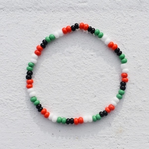 Puede incluir: Un brazalete de cuentas de colores con cuentas negras, blancas, verdes y naranjas.