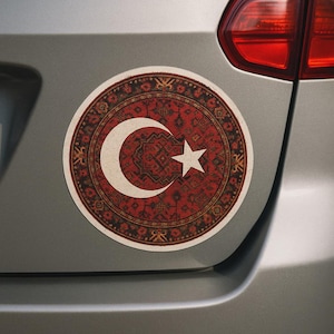 Può includere: Un adesivo rotondo con un design di tappeto turco tradizionale in rosso, beige e oro. Presenta una luna crescente e una stella bianche, simboli della Turchia, sullo sfondo del motivo del tappeto.