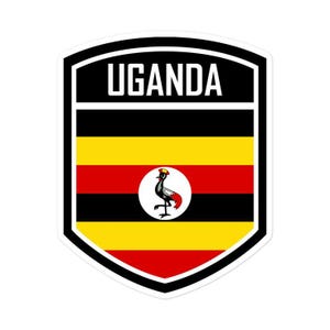 May include: A shield-shaped sticker featuring the national flag of Uganda with horizontal stripes of black, yellow, and red. The word UGANDA is printed in white capital letters at the top, and a grey crowned crane is centred in a white circle.