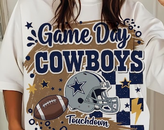 Peut inclure: T-shirt blanc avec un motif "Game Day Cowboys". Le design comprend un ballon de football américain, un casque avec une étoile et le mot "Touchdown". Le t-shirt a une coupe ample et des manches courtes.