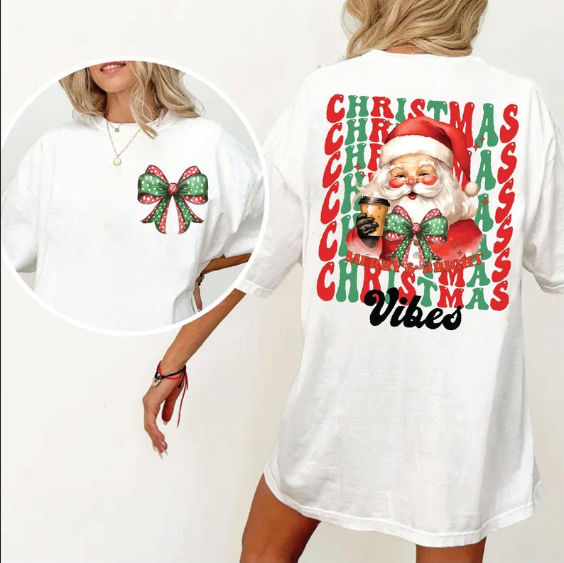 May include: White oversized t-shirt with a red and green Christmas design. The design features a cartoon Santa Claus holding a cup of coffee and a bow. The text "Christmas Vibes" is printed in black below the design.
