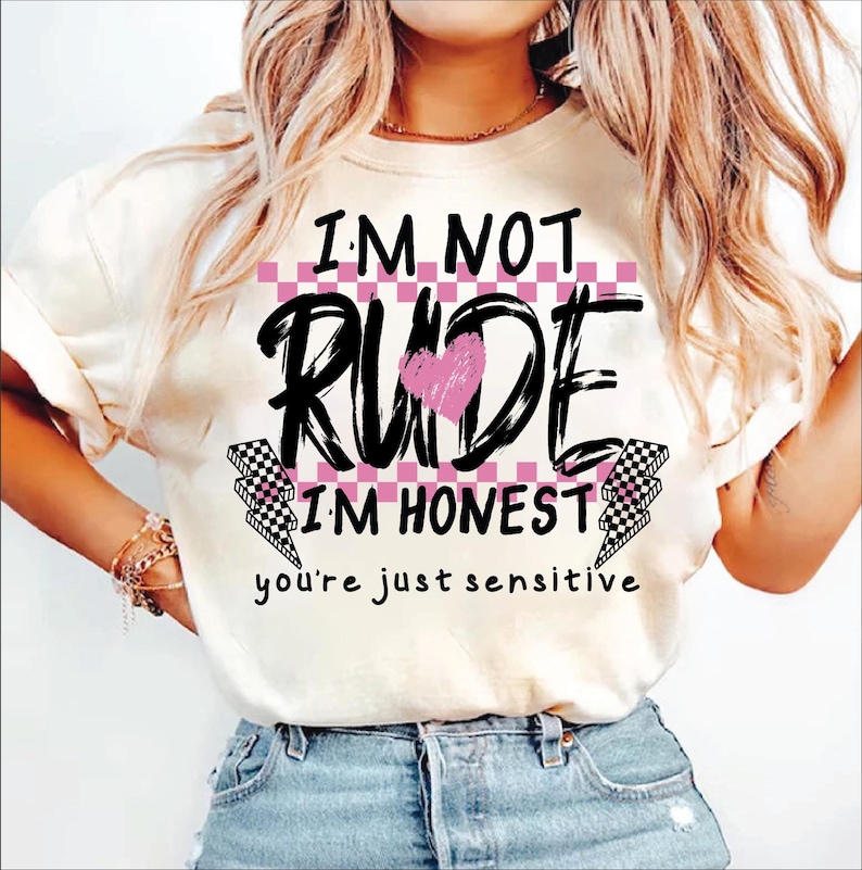 May include: White t-shirt with black text that reads "I'm not rude I'm honest you're just sensitive". The text is surrounded by a pink and black checkered pattern and a pink heart.