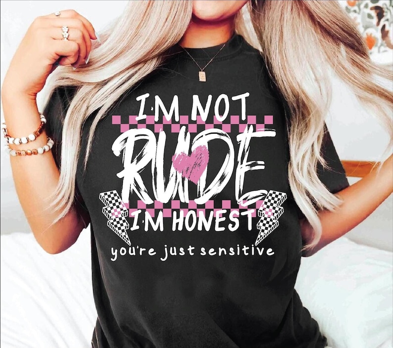 May include: Black t-shirt with a white graphic that says "I'm not rude I'm honest you're just sensitive". The graphic includes a pink heart and checkered pattern.