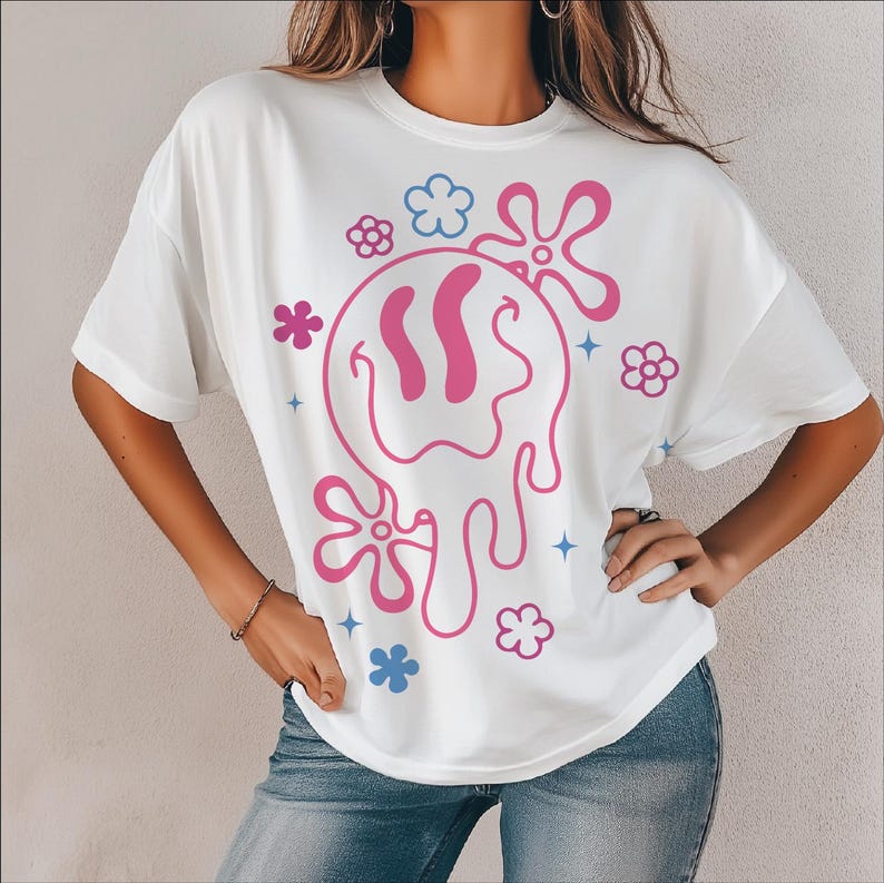 Peut inclure: T-shirt blanc avec un motif graphique rose et bleu d'un visage souriant fondant et de fleurs.