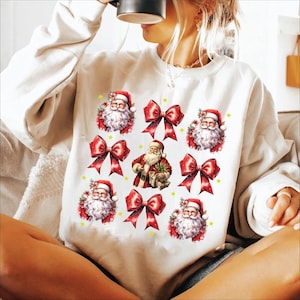 Puede incluir: Sudadera blanca con un dise&ntilde;o navide&ntilde;o festivo con m&uacute;ltiples im&aacute;genes de Pap&aacute; Noel y lazos rojos.