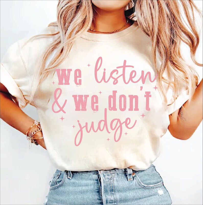 May include: A white t-shirt with a pink graphic that says "We listen & We don't judge".