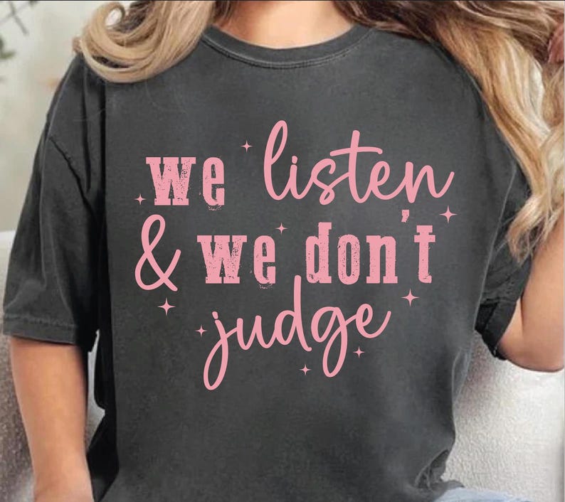 May include: A dark gray t-shirt with the text "We listen & we don't judge" printed in pink.