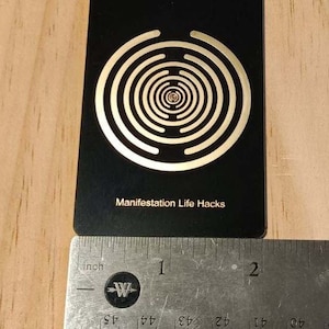 May include: Black card with a gold concentric circle design and the text "Manifestation Life Hacks".