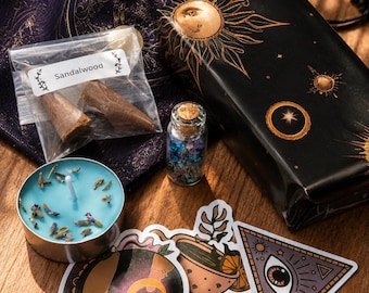 May include: A collection of items including a purple drawstring bag, a black box with gold sun and star illustrations, a clear plastic bag labeled Sandalwood containing two incense cones, a small glass vial with cork, a blue tea light candle, and three stickers.