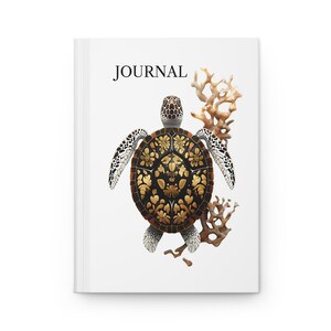 May include: A white journal cover with the word "JOURNAL" printed in black at the top. A black and white sea turtle with a gold patterned shell is centered on the cover. The turtle is surrounded by brown coral.